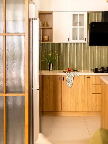 Natural light and earthy textures define this kitchen. Light wood cabinets are paired with a green subway tile backsplash, and a fluted glass partition door allows light to flow through from the living area.