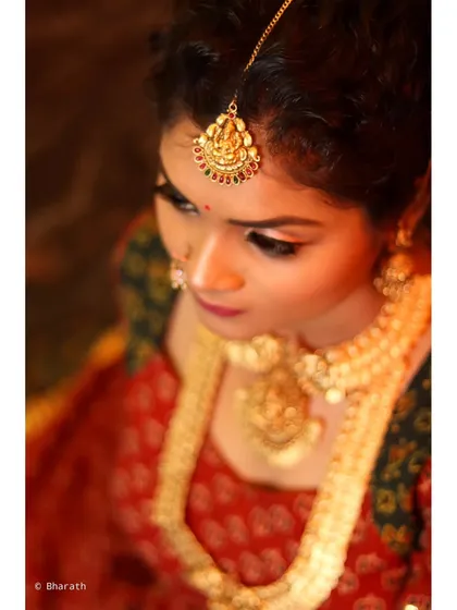 A high-angle shot of a model in a traditional printed lehenga. This perspective emphasizes the intricate gold jewelry, including the maang tikka and layered necklaces, creating a rich, regal portrait.