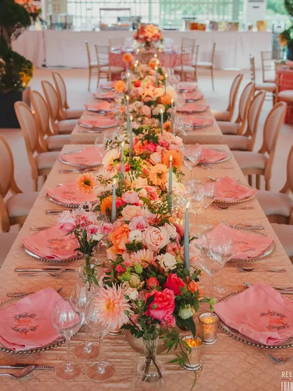 An elegant long-table setup for a reception in the UK. The runner of fresh flowers and tapered candles creates a romantic and sophisticated tablescape.