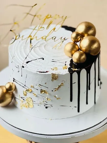 A chic white cake with black drips and gold spheres, a modern and stylish choice for any birthday.