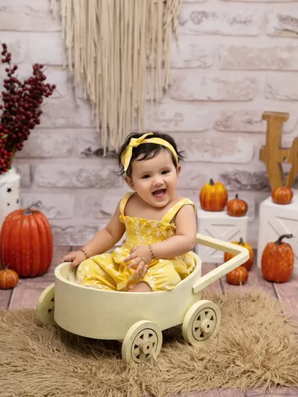 The joy of a sunny day at the pumpkin patch. Her bright smile matches her yellow outfit perfectly in this cheerful autumn-themed milestone session.