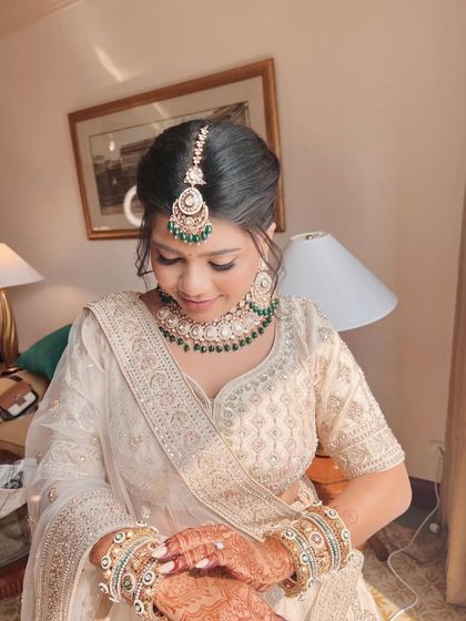 A classic white lehenga paired with a timeless, elegant makeup look. The focus is on a clean, low bun with fresh flowers and a soft, natural glow.