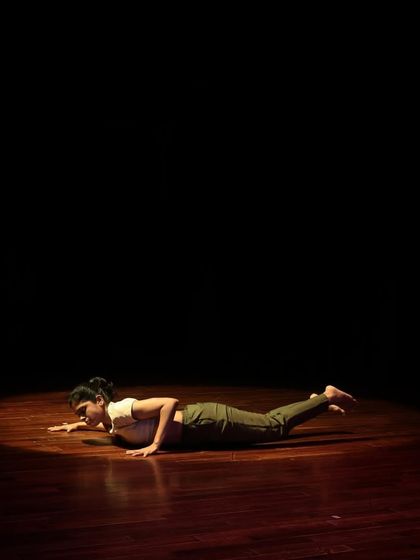 A contemporary dancer lies on the stage, using the floor as part of her expressive choreography.