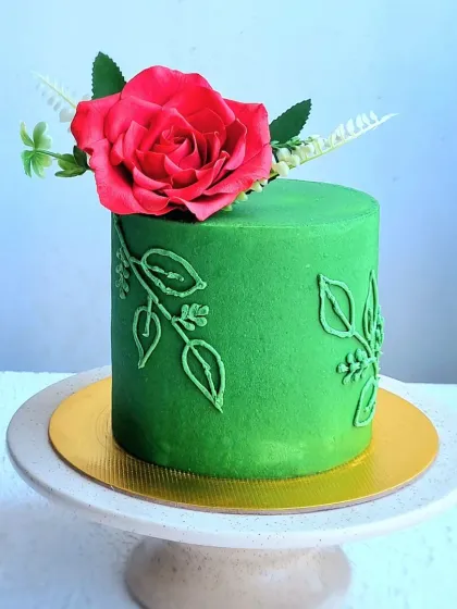 A simple but striking buttercream cake. This design features a vibrant green color, a piped leaf pattern, and a single, beautifully crafted red sugar rose.
