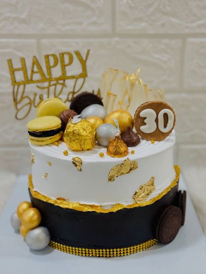 A stylish black and white cake for a 30th birthday. This design is topped with macarons, Ferrero Rocher, and gold leaf for a sophisticated and celebratory look.