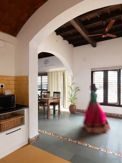 A glimpse of the interiors of the Basavanagudi house, showing the seamless flow between the kitchen, dining, and living areas. The use of arches and natural materials creates a sense of warmth and openness throughout the home.