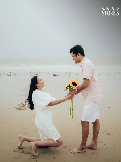 A playful and romantic proposal moment on the sand, with sunflowers adding a bright, cheerful touch to this casual beach pre-wedding shoot.