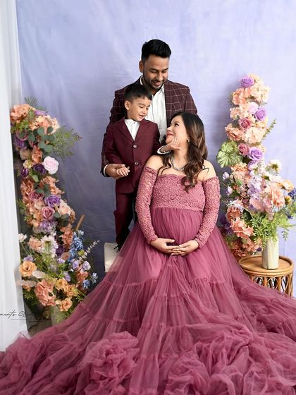 A beautiful family portrait with the son looking lovingly at his mother's baby bump. The coordinated outfits and floral setting create a soft and romantic atmosphere for this maternity session.