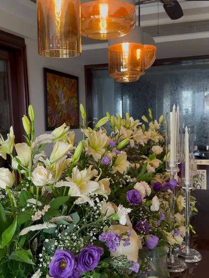 A close up of a floral centerpiece under modern amber glass pendant lights. The warm lighting enhances the colors of the flowers and creates a cozy atmosphere.