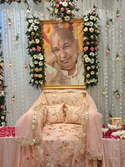 This is a complete altar setup for a Guru Ji satsang. I used columns of white and pink flowers to frame the space, with a sheer curtain backdrop and a decorated throne featuring custom 'Om' pillows. The focus is on creating a serene and devotional atmosphere.