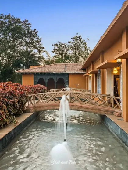 The beautiful heritage-style architecture of Vijayshree Resort, with a fountain and a small bridge connecting different sections of the property. The warm, earthy tones of the building glow in the evening light.