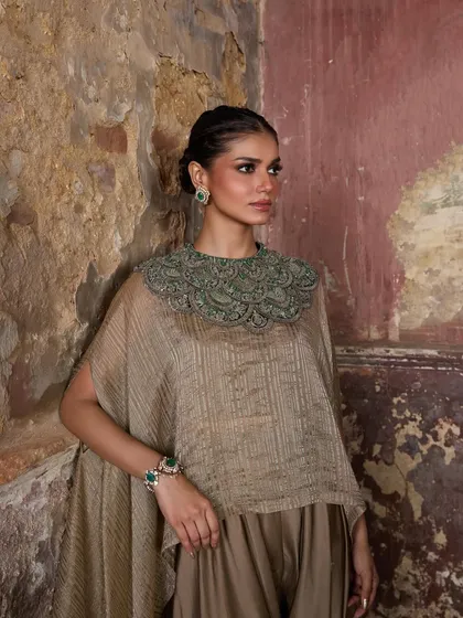 A timeless tale of textures and tones. This model wears a striped cape with a heavily embellished green collar over matching pants, a perfect blend of structure and flow.