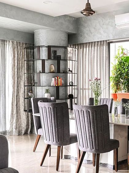 This wide shot shows how the living and dining areas flow together in an open-plan layout. The consistent use of a grey and neutral palette, punctuated by thoughtful details like the custom column bookshelf, creates a harmonious and expansive feel.