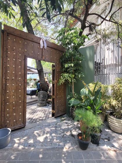 The entrance gate is framed by lush greenery, giving a hint of the garden oasis that lies within. This threshold moment is designed to be an invitation to leave the city behind and enter a different world.