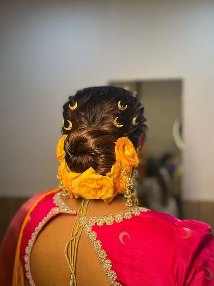 A twisted bun adorned with vibrant yellow roses and delicate moon-shaped pins. This hairstyle is a cheerful and modern choice, perfect for a Haldi ceremony or a bride who loves a pop of color.