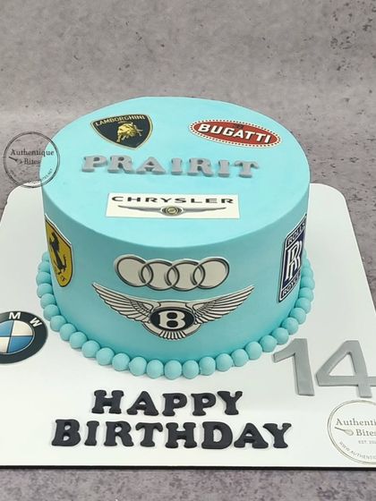 A car lover's dream cake, decorated with the logos of iconic car brands like Lamborghini, Bugatti, Ferrari, and Bentley.