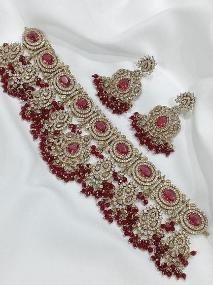 This choker set is available in multiple colors including ruby, emerald, and grey. The intricate metalwork combined with colored stones and pearl or bead droppings offers a sophisticated and royal look.