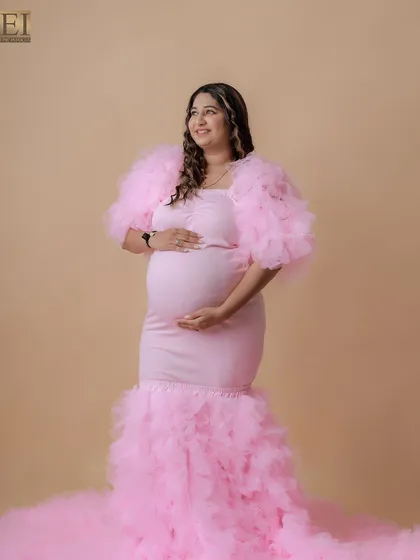 A beautiful full-length shot of a mom-to-be in a stunning pink mermaid-style gown with a dramatic ruffled train.