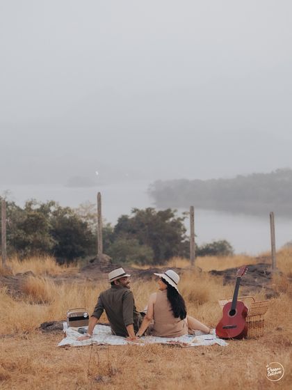 A couple enjoying a conversation during their picnic by the lake. This wide shot captures the peaceful ambiance and the beauty of the Lonavala landscape, setting a perfect scene for their story.