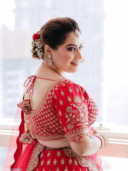 A beautiful back profile of Sakshi, showing her elegant bridal bun adorned with red roses. The hairstyle perfectly complements her traditional red lehenga.