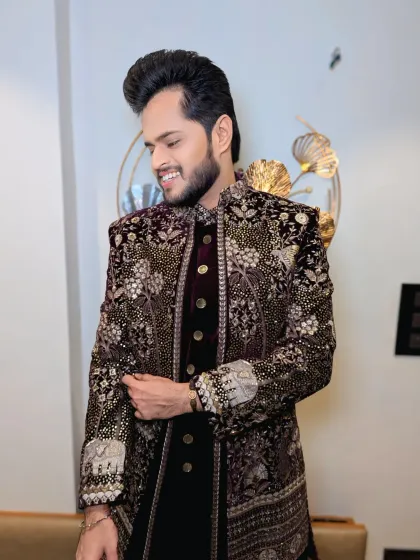 A stunning, heavily embroidered velvet sherwani for a grand Sangeet or reception. The hairstyle is voluminous to balance the regal outfit.