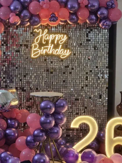 A close-up of the 26th birthday sequin wall, showing the neon sign and the metallic sheen of the purple balloons.