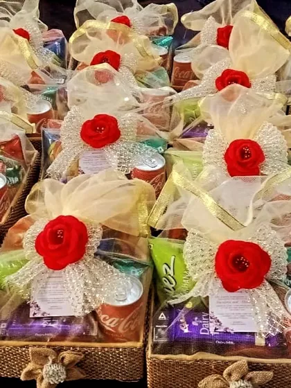 A still image of the sweet and savory room hampers. The red rose and beaded bow add a touch of luxury, while the visible contents like Coca-Cola and chips promise a comforting and enjoyable treat for guests.