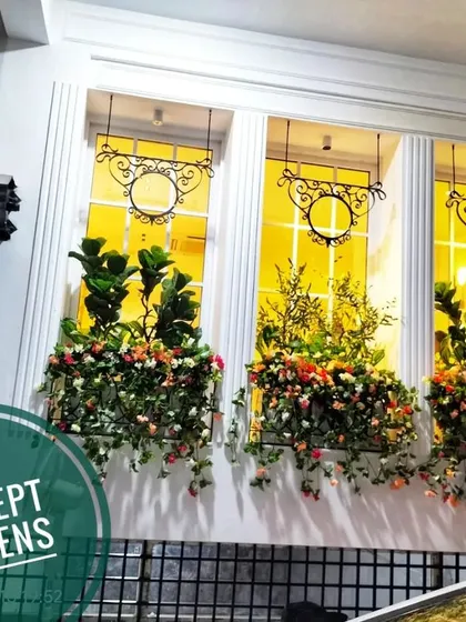 The restaurant's artificial flower boxes seen at night. The warm interior lighting makes the windows glow, highlighting the floral arrangements.