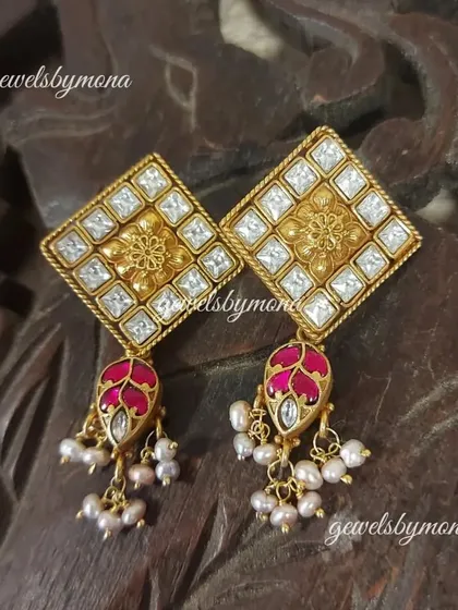 Another beautiful pair of Dakshinaya earrings, featuring a diamond-shaped polki stud with a floral gold center and a delicate ruby-colored jhumki drop surrounded by pearls.