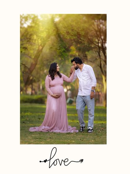A gentle and chivalrous moment in a sun-drenched park. The partner kisses the expecting mother's hand, a simple gesture of love captured during their outdoor maternity session.