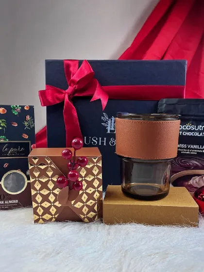 The 'Cozy at Home' hamper is perfect for a relaxing Christmas. It includes dark almond chocolate, Swiss vanilla hot chocolate mix, and a stylish glass tumbler with a leather-finish sleeve.
