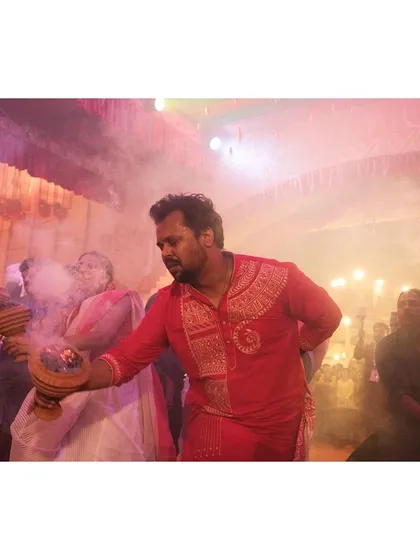 A man in a traditional red kurta leads the Dhunuchi dance, enveloped in the fragrant smoke from the censer.