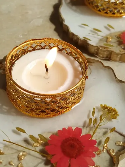 This is a close-up of my resin floral diya. The base is made of white resin with preserved red flowers and gold flakes, and it holds a golden filigree tea light holder.