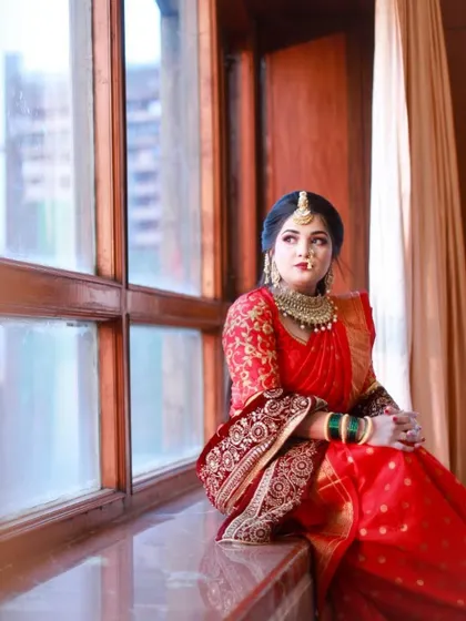 The bride by the window, with natural light highlighting her flawless makeup and the rich color of her saree.