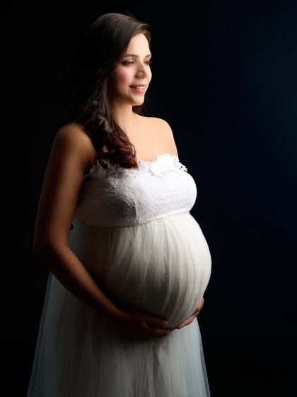 A classic bust-up portrait using Rembrandt lighting to create depth and drama. The focus is entirely on the mother-to-be's serene expression and the beautiful contours of her form.