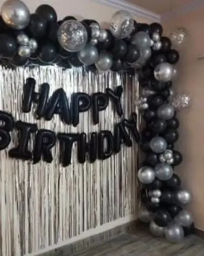 A stylish black and silver balloon frame with a fringe curtain, perfect for a modern birthday celebration at home.