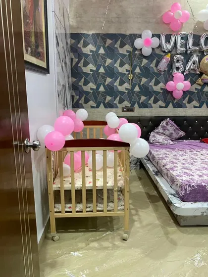 A close-up of a beautifully decorated nursery crib, ready for the new baby. Simple clusters of pink and white balloons add a touch of celebration to the baby's first bed.