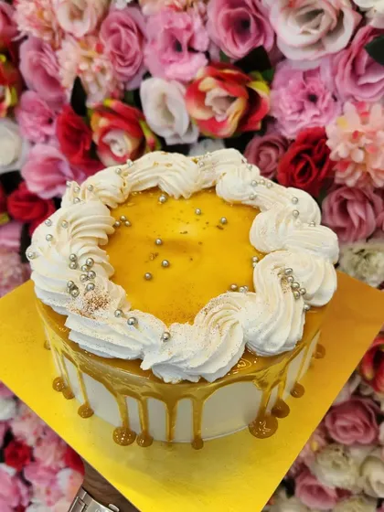 A delicious Caramel cake with a beautiful golden drip. The top is adorned with swirls of whipped cream and silver pearls, making it an elegant choice for any celebration. The sweet and buttery caramel flavor is simply irresistible.