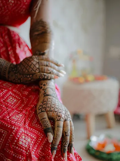 A detail-oriented shot focusing on the bride's hands, covered in elaborate mehndi. Her red outfit provides a beautiful contrast to the dark henna.