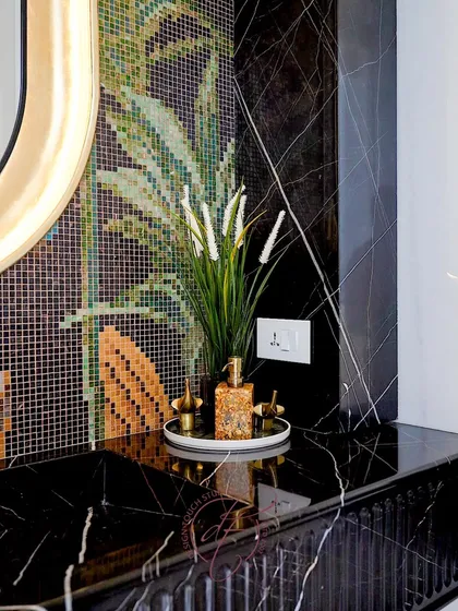 A close-up of the black marble vanity and the vibrant mosaic wall. The gold-toned accessories and artificial plant add a touch of elegance and freshness to the dramatic design.