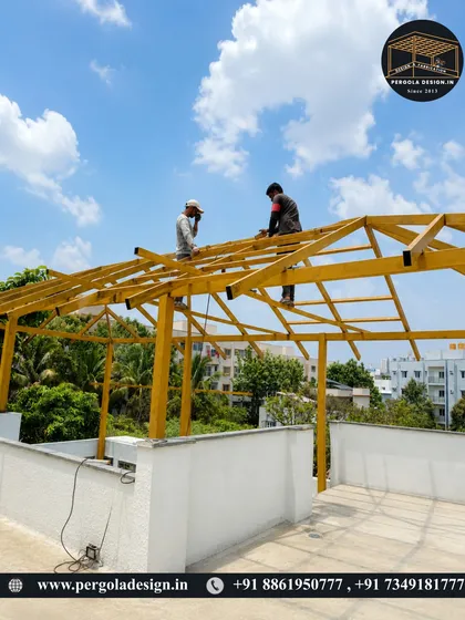 Two workers carefully position and secure the rafters of the pergola roof.