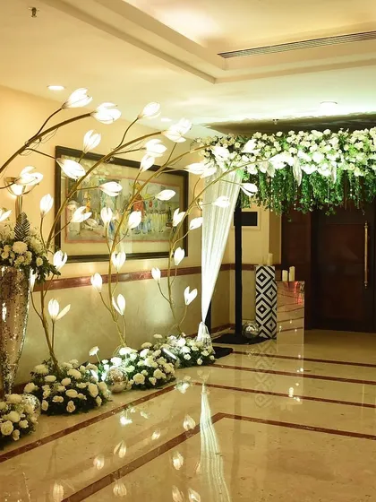 An elegant and artistic entrance detail. Glowing, flower-like light installations are arranged alongside classic white floral bouquets, creating a magical and contemporary welcome.