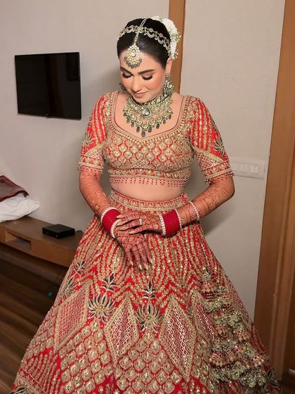 A full view of this bride's stunning red lehenga and intricate jewelry. The makeup is designed to balance these elements, creating a cohesive and breathtaking overall look.