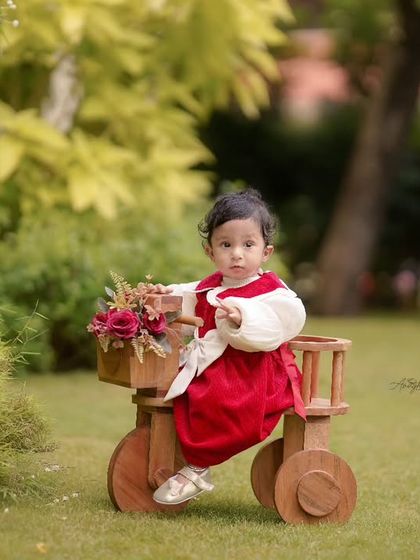 A toddler milestone session in a garden. Using props like this wooden tricycle adds a playful element to outdoor photoshoots for little ones.