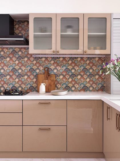 This kitchen features a beautiful, intricate patterned tile backsplash that serves as the focal point. The glossy beige cabinets and reeded glass upper shutters create a warm, contemporary look that is both elegant and low-maintenance.