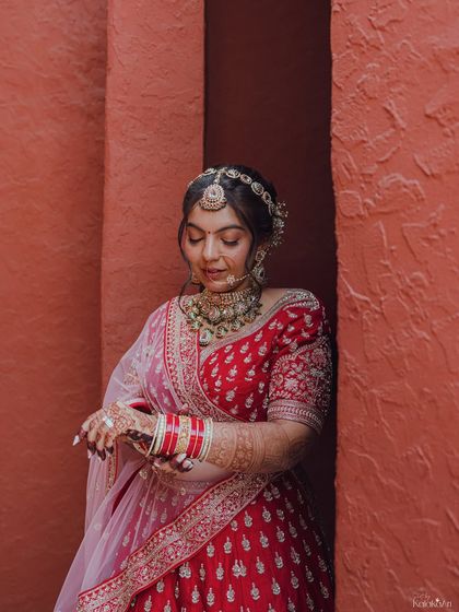A classic bridal portrait, with the bride adjusting her bangles. This shot highlights her intricate jewelry and the rich color of her lehenga.