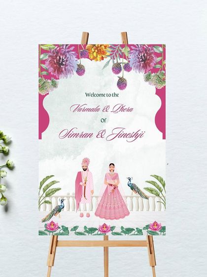 This magnificent welcome signage for the Varmala and Phera ceremony features a beautiful couple illustration in pink attire. The design is framed by lush florals, peacocks, and traditional Indian architecture for an elegant welcome.