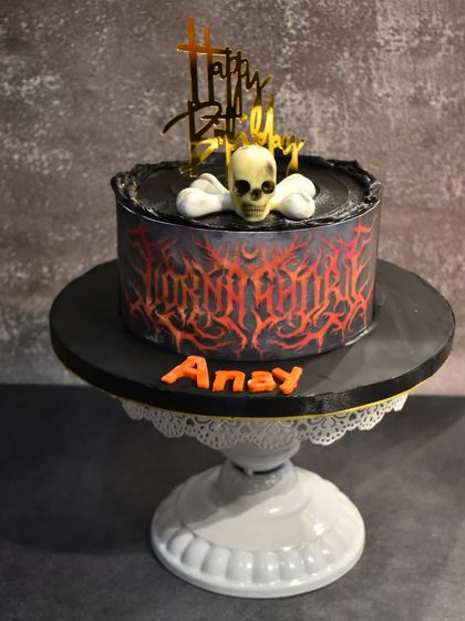 A cake that rocks. This edgy design for a metal music fan features a fiery airbrushed pattern, a skull and bones topper, and a dark chocolate ganache flavor.