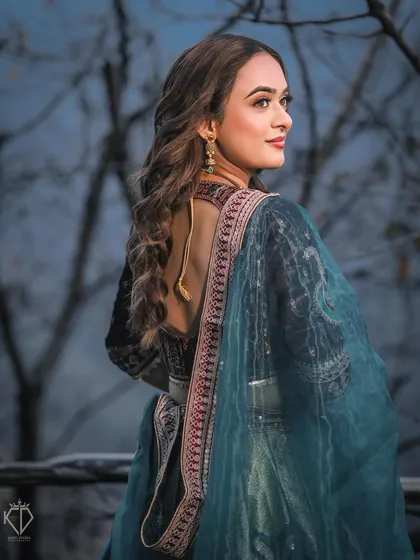 A classic back-pose portrait of the bride, showcasing her elegant hairstyle and the detailed embroidery of her outfit.