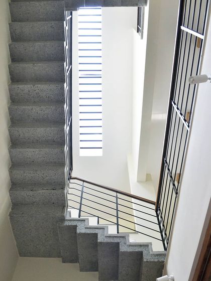 A view looking down the stairwell, where a tall, narrow window allows light to penetrate deep into the house while maintaining privacy.